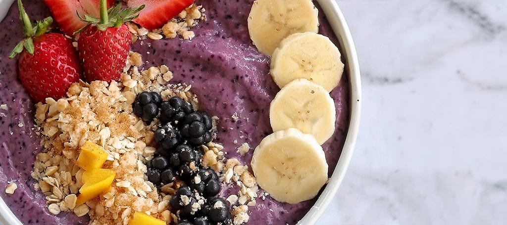 An açaí bowl and several healthy side dishes on a white marble table