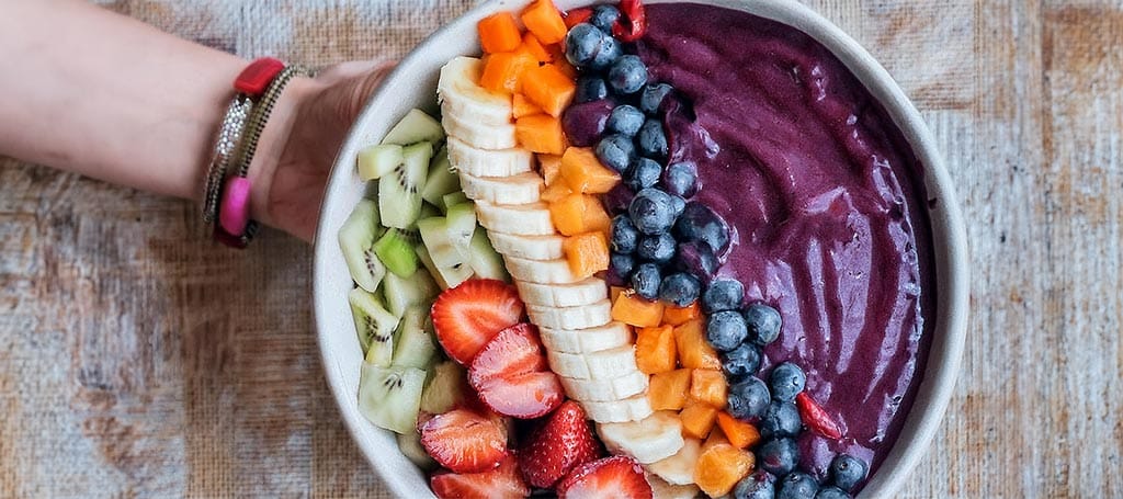 A beautiful açaí bow with various fruits being held by a young woman