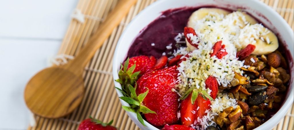 Acai bowl, with fruits, cereals, banana. A wooden spoon on the side.