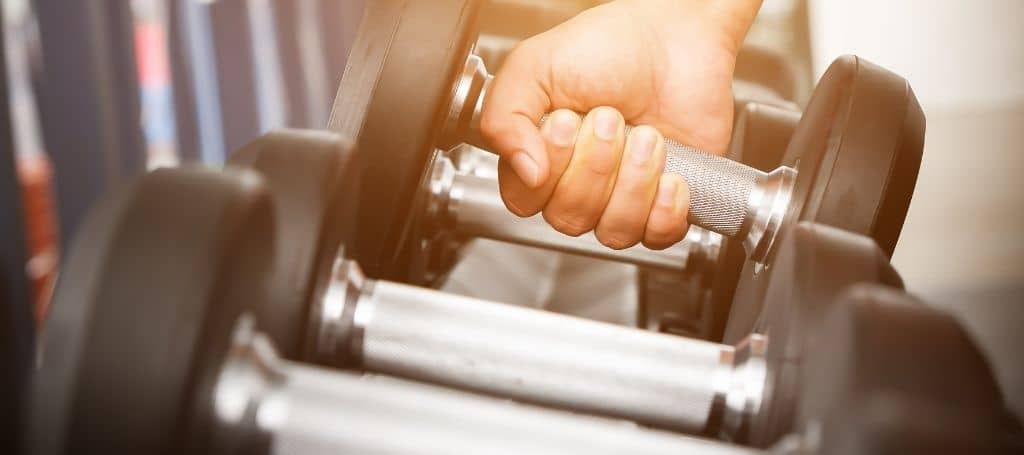 Close up photo of a hand picking up one of the dumbbells on the rack in a gym