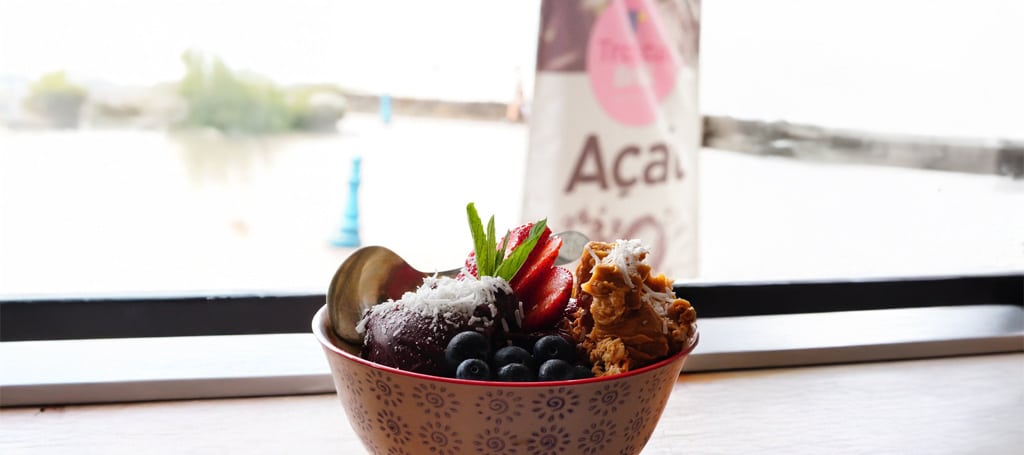 Açaí Bowl with fruits, and in the background a flag with the Tropical Brazil logo