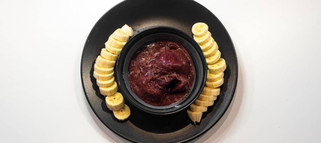 black plate with a bowl of açaí, and bananas around it