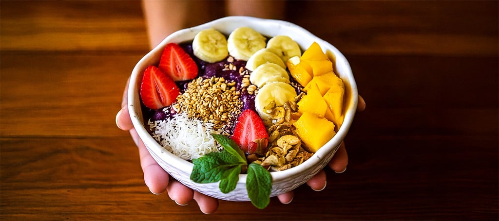 hands of a person holding an acai bowl with fruits